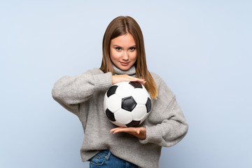 Teenager girl with sweater over isolated blue background holding a soccer ball