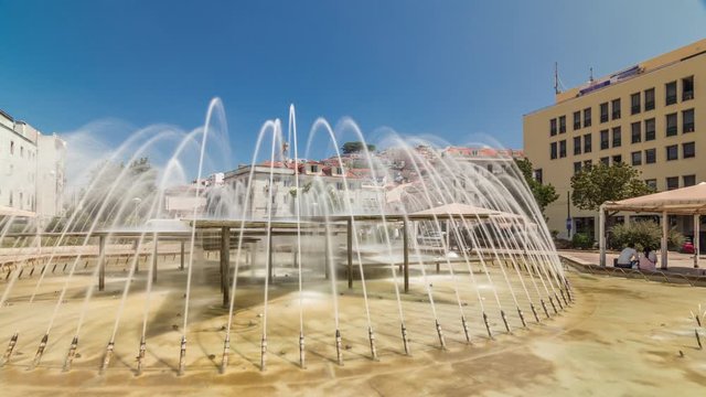 Fountain in Martim Moniz square timelapse hyperlapse in downtown Lisbon. Historic buildings on hills on a background with blue sky