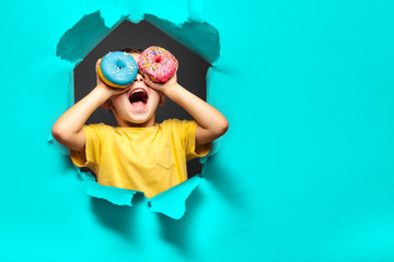 Happy cute boy is having fun played with donuts on black background wall.