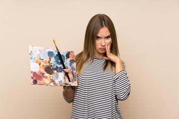 Teenager girl holding a palette over isolated background unhappy and frustrated