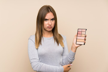 Teenager girl with makeup palette over isolated background with sad expression