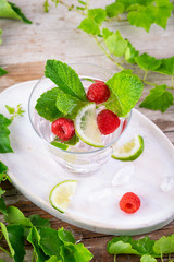 Summer fresh drink. Raspberry mint alcohol cocktail, slice of lime, ice cubes and raspberry on a natural wooden surface, Outdoor. Copy space.