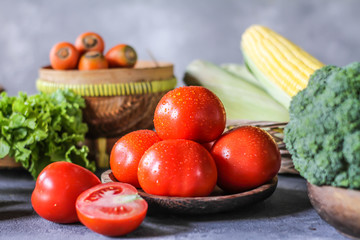 Photo of fresh tomatoes in a bowl on dark background around vegetables, carrot, salt, black pepper, corn, broccoli. Slice tomatoes. Harvesting tomatoes. Drops of water vegetables. Wooden table. Image