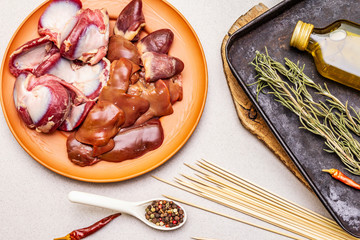 Fresh raw duck offal: heart, liver, stomach. Dry spices, rosemary, chili, oil. Baking tray, wooden skewers, stone concrete background