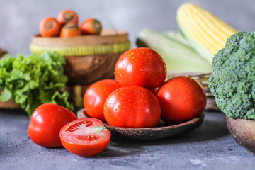 Photo of fresh tomatoes in a bowl on dark background around vegetables, carrot, salt, black pepper, corn, broccoli. Slice tomatoes. Harvesting tomatoes. Drops of water vegetables. Wooden table. Image