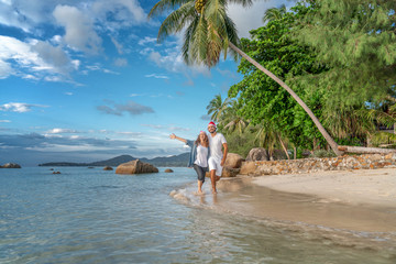 Young beautiful couple in Santa Claus hats walks along the shore of the tropical sea at the resort,...