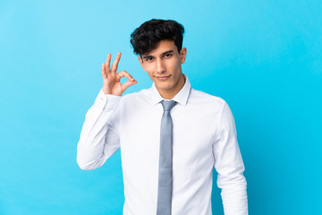 Young Argentinian businessman over isolated blue background showing an ok sign with fingers