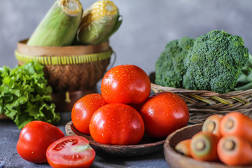 Photo of fresh tomatoes in a bowl on dark background around vegetables, carrot, salt, black pepper, corn, broccoli. Slice tomatoes. Harvesting tomatoes. Drops of water vegetables. Wooden table. Image