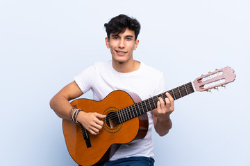 Young Argentinian man with guitar over isolated blue background