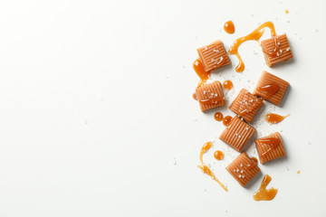 Salted caramel candies and sauce on white background, space for text