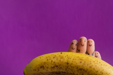 Painted funny fingers smiley holding yellow banana against purple background