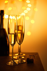 cork, bottle and glasses with sparkling wine, with yellow christmas lights bokeh