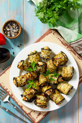 Appetizer stuffed with eggplant. Fried eggplant roll with feta cheese and nuts in a plate on a wooden kitchen table. Top view on a flat background. Copy space.