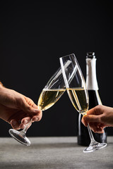 cropped view of couple clinking with glasses and celebrating christmas, on black with bottle of champagne