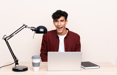 Young Argentinian man in a table with a laptop in his workplace with surprise facial expression