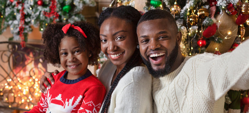Cheerful afro family taking selfie while celebrating Christmas at home