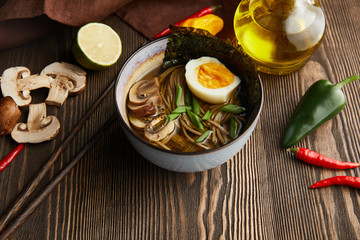 traditional spicy ramen in bowl with chopsticks and vegetables on wooden table with napkin