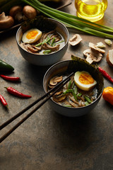 traditional spicy ramen in bowls near chopsticks and vegetables on stone surface