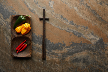 top view of chopsticks and fresh peppers on stone surface