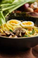 close up view of traditional spicy ramen in bowl on brown napkin on stone surface