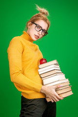 blonde girl in a yellow sweater holds a stack of books on a green background