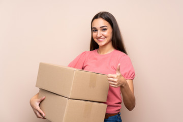 Young woman over isolated background holding a box to move it to another site with thumb up