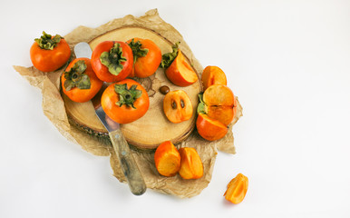 Persimmon lies on a wooden Board on a white background. Persimmon close - up whole and cut into slices with a knife. Organic farming, healthy food concept, eco-friendly products, vegetarian, raw 