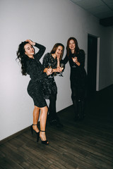 Party, holidays, celebration, nightlife people concept. New year celebration party in the club. Three beautiful women in black sparklers night fashion dress holding wineglass of alcohol