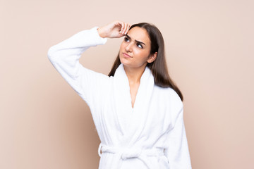 Young girl in a bathrobe over isolated background having doubts and with confuse face expression