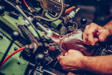 Hands of an Experienced shoemaker using a special machine for putting shoes on the mold, in the...