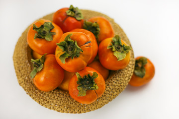 Persimmon closeup lying in a bowl hat on a white background. Organic farming, healthy food concept, eco-friendly products, vegetarian, raw products.