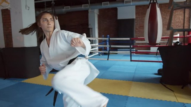 Young Caucasian female martial arts fighter training punches and kicks inside boxing ring