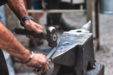 An artisan blacksmith knocks with a hammer on iron to shape