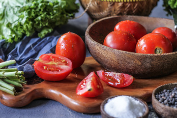 Photo of fresh tomatoes in a bowl on dark background around vegetables, carrot, salt, black pepper, corn, broccoli. Slice tomatoes. Harvesting tomatoes. Drops of water vegetables. Wooden table. Image