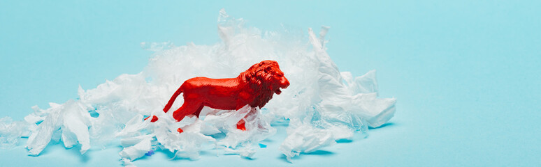 Panoramic shot of red toy lion with plastic garbage on blue background, animal welfare concept