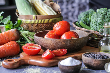 Photo of fresh tomatoes in a bowl on dark background around vegetables, carrot, salt, black pepper, corn, broccoli. Slice tomatoes. Harvesting tomatoes. Drops of water vegetables. Wooden table. Image