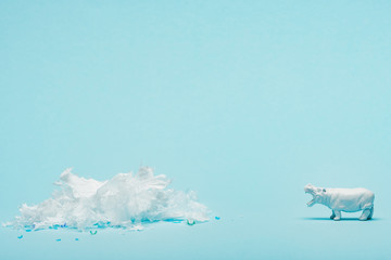 White hippopotamus toy and plastic garbage on blue background, animal welfare concept