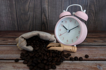 Coffee beans are in brown sacks on brown wood  ground near the pink alarm clock.