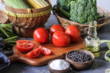 Photo of fresh tomatoes in cutting board on dark background, around vegetables, carrot, salt, black pepper, corn, broccoli. Slice tomatoes. Harvesting tomatoes. Wooden table. Image