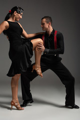 sensual dancer touching leg of partner while dancing tango on grey background