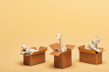 White toy hippopotamus, rhinoceros and giraffe in cardboard boxes on yellow background, animal welfare concept