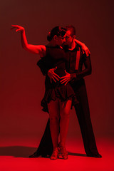 elegant couple of dancers in black clothing performing tango on dark background with red illumination