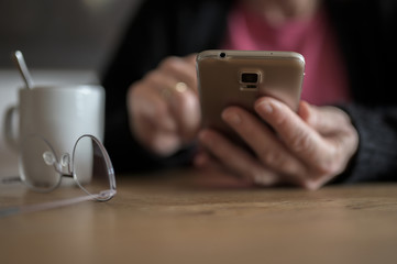 Someone typing something on her phone at the table with a cup of coffee and reading glasses on it.