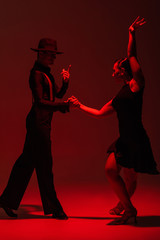 elegant couple of dancers in black clothing performing tango on dark background with red...