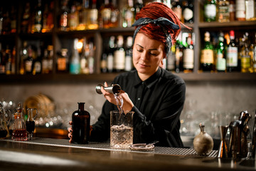 Bartender girl with a red hair pouring a alcoholic drink from the jigger to a measuring glass cup
