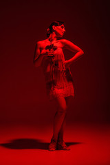 beautiful tango dancer in dress with fringe holding rose on dark background with red illumination