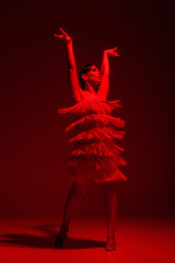 beautiful dancer in dress with fringe dancing tango on dark background with red illumination