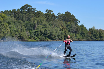 Young man water skiing over the river in summer, having fun