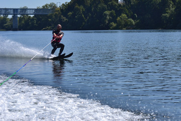 Young man water skiing over the river in summer, having fun