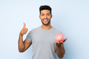 Young handsome man over isolated background holding a big piggybank